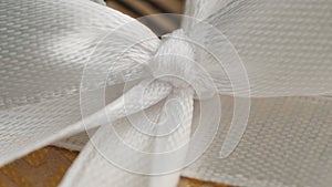 White ribbon bow on yellow gold gift box background. Extreme close-up of a knot. Macro view. Soft focus, depth of field