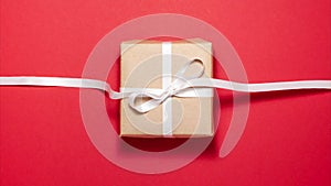 White ribbon tied in a gift bow on brown paper gift box on red background. Flat lay top view stop motion animation
