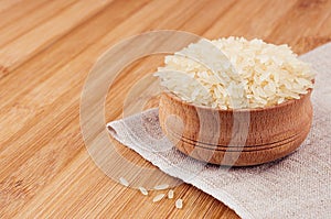 White rice basmati in wooden bowl on brown bamboo board, closeup. Rustic style, healthy dietary cereals background.