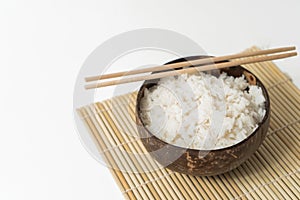 White rice in a coconut bowl on a white background. Minimalistic photo with rice and bamboo chopsticks