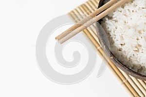 White rice in a coconut bowl on a white background. Minimalistic photo with rice and bamboo chopsticks