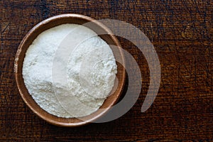 White rice flour in dark wooden bowl isolated on dark brown wood