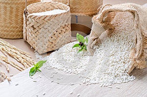 White rice grains in burlap bag and basket on wooden background