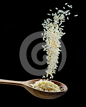 White rice grains falling down into the spoon at black background. Popular food and main ingredient of risotto and pilau