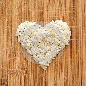 White rice grains in heart shape on wooden cutting board, in square format for social media, banners, and backgrounds.