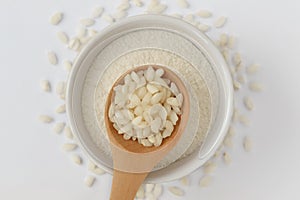 White rice grains on wooden spoon and rice flour in bowl