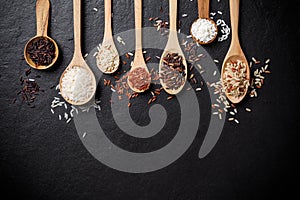 White rice, Jasmine rice, Black rice, Brown rice, Riceberry and Mixed rice in wooden spoon over black table background with copy