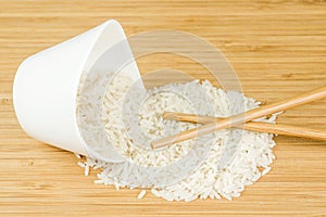 White rice spill out of wite ceramic bowl with two bamboo sticks