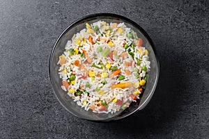 White rice with vegetables in a black bowl on black background