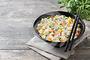 White rice with vegetables in a black bowl on wooden table