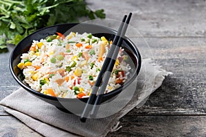 White rice with vegetables in a black bowl on wooden table