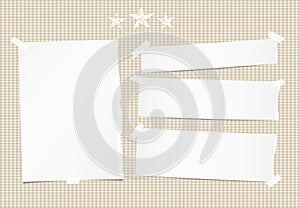 White ripped note, notebook, copybook paper sheet, strips and stars on brown squared background. photo