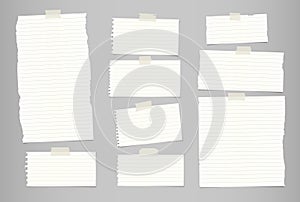 White ripped striped note, notebook paper for message or text stuck with sticky tape on gray background.