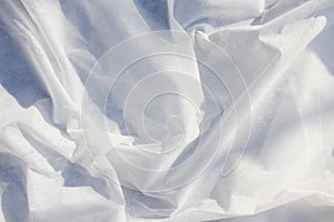 White rippled textured fabric background illuminated by the rays of the sun. Luxurious background design