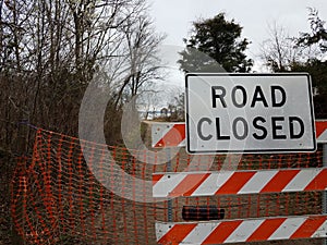 White road closed sign and striped barricade with trail or path