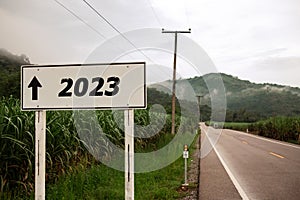 white roadside sign says 2023 with an arrow pointing straight ahead.