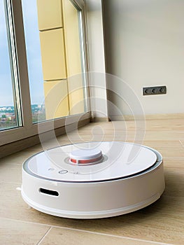 White robot cleaner. Robot vacuum cleaner on laminate floor in action