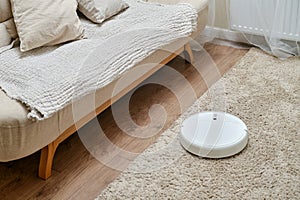 White robot vacuum cleaner on a fleecy carpet, home interior