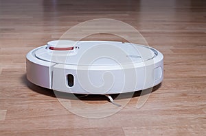 white robot vacuum cleaner on parquet floor cleaning dust in the room. smart robotic automate wireless cleaning technology