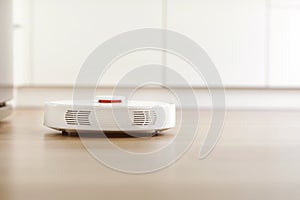 White robotic vacuum cleaner on laminate floor cleaning dust in living room interior. Smart electronic housekeeping