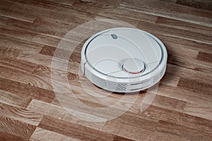 White robotic vacuum cleaner runs on laminate floor. Robot controlled by voice commands for direct cleaning. Modern smart