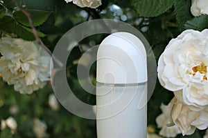 White roll-on antiperspirant deodorant in the glass bottle and white roses on the blurred natural green background
