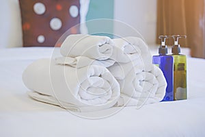 white rolled towel , blurred bath accessories bottles on cleaned bed in bedroom