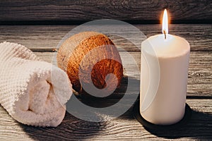 White rolled towel with coconut and burning candle on wooden table.