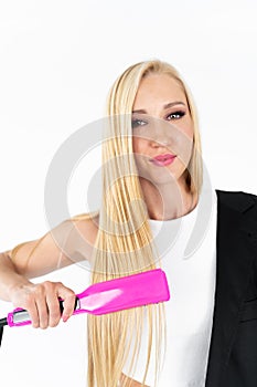 In a white room, a stylish blonde woman with long hair in black straightens her long blonde hair wit