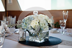 White roses and blue hydrangea in  square glass vase on light tablecloths with navy blue placemats