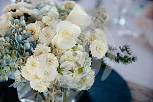 White roses and blue hydrangea in  square glass vase on light tablecloths with navy blue placemats