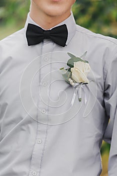 White roses flowers in buttonhole, the grooms friend is dressed in a grey shirt and a bow tie. Wedding day. Outfit of the day