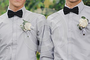 White roses flowers in buttonhole, two grooms friends is dressed in a grey shirt and a bow tie. Wedding day. Outfit of the day