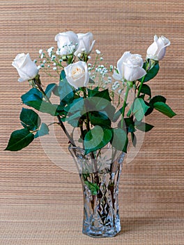 White roses with green leaves in a glass vase with water