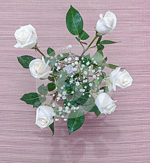 White roses with green leaves in a glass vase with water