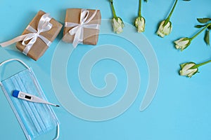 white roses  medical mask  thermometer  gifts in craft paper tied with a white satin ribbon on a bluebackground.