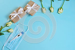 white roses  medical mask  thermometer  gifts in craft paper tied with a white satin ribbon on a bluebackground.
