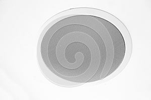 White speaker and grille hanging on white ceiling.