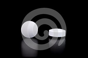 White round pharmaceutical pills on reflective surface, black background