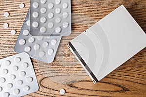 White round pills in aluminum packaging and white box of pills on a wooden table, copy space