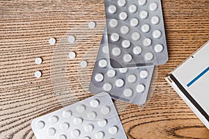 White round pills in aluminum packaging and white box of pills on a wooden table, copy space