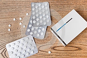 White round pills in aluminum packaging and white box of pills on a wooden table, copy space