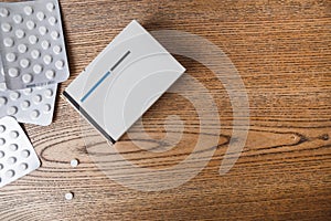 White round pills in aluminum packaging and white box of pills on a wooden table, copy space