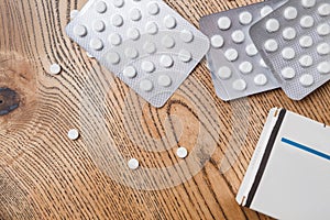 White round pills in aluminum packaging and white box of pills on a wooden table, copy space