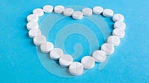 White round pills laid out in the shape of a heart on a blue background. Health symbol made of pills for therapy, treatment and