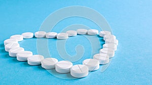 White round pills laid out in the shape of a heart on a blue background. Health symbol made of pills for therapy, treatment and
