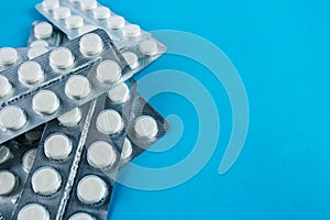 White round pills in pack. Tablets are next to the packaging on a blue background