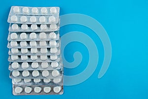 White round pills in pack. Tablets are next to the packaging on a blue background