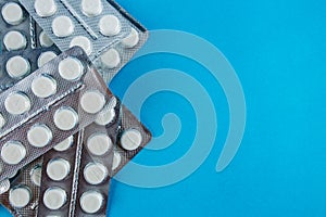 White round pills in pack. Tablets are next to the packaging on a blue background