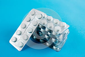 White round pills in pack. Tablets are next to the packaging on a blue background